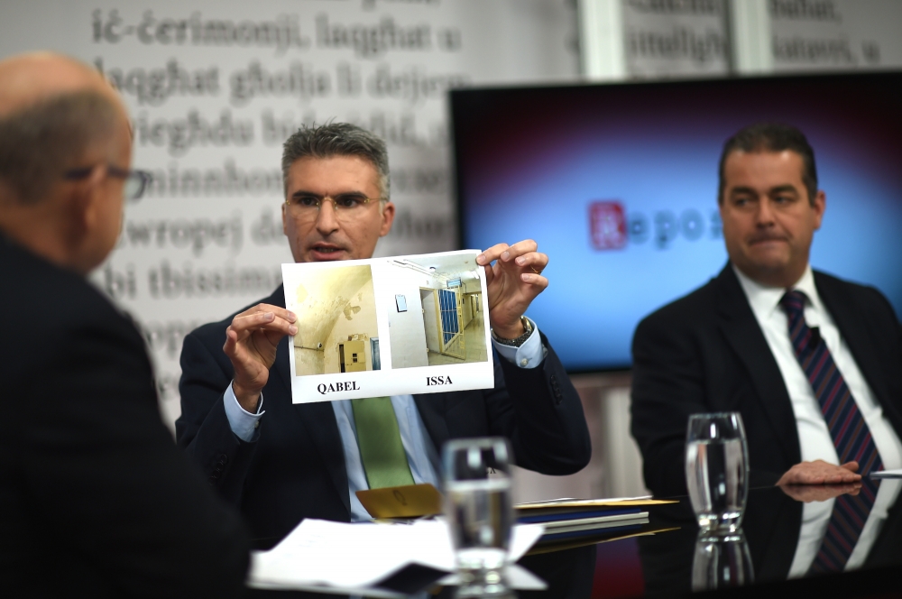Minister Carmelo Abela displays pictures comparing current and past conditions of police lock-up. Photo: Ray Attard