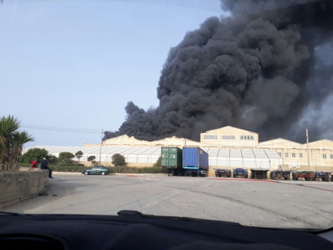 Large plumes of black smoke can be seen coming out of the factory as the building's roof burns