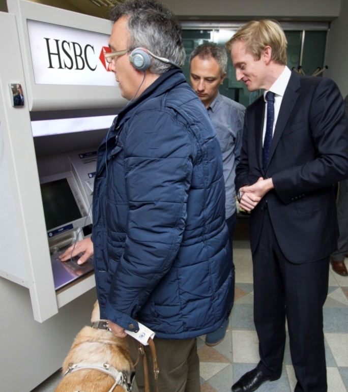 Visually impaired HSBC customer Joseph Stafrace, accompanied by his guide dog, trying his hand on the bank’s Talking ATM as Gordon Gilford and Andrew Beane look on