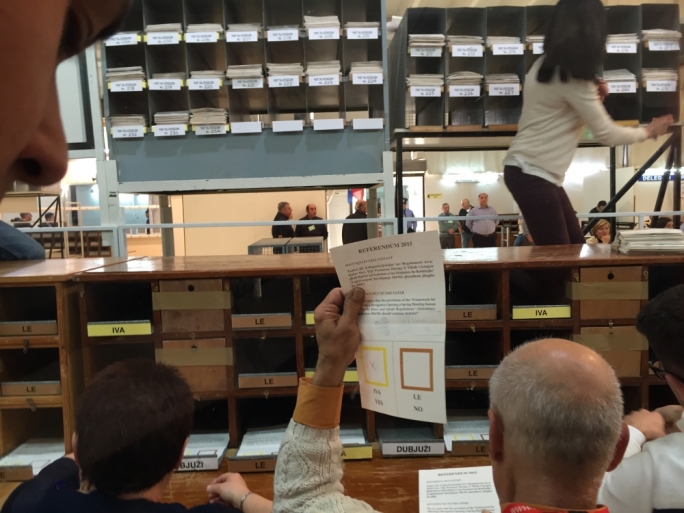 Counting staff lift their votes up high so that monitors inspect the process from behind the perspex wall.