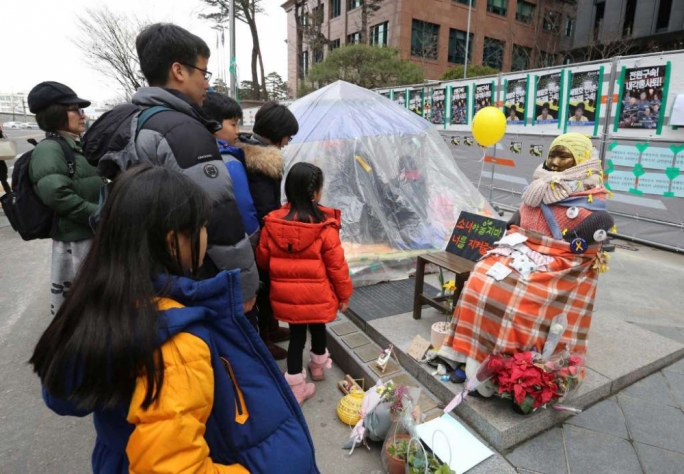 People watch a statue symbolizing women forced into wartime Japanese military brothels in front of the Japanese Embassy in Seoul