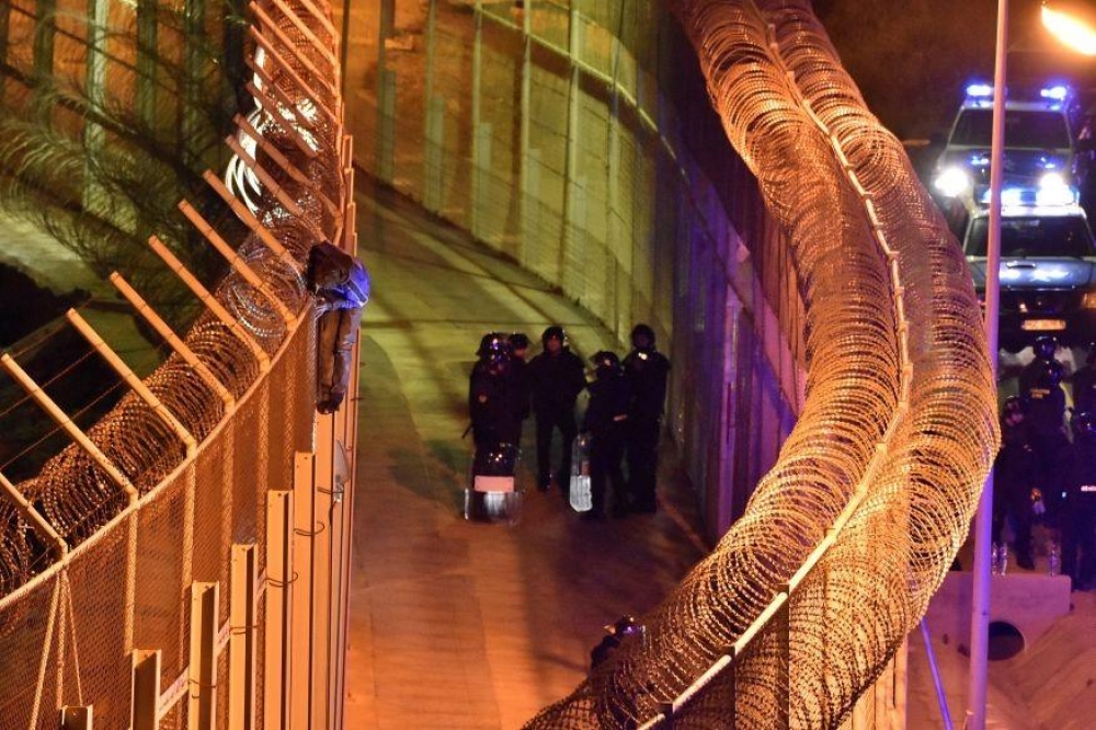 Spanish border guards look on as a migrant attempts to climb the fences in Ceuta (Photo: Reuters)